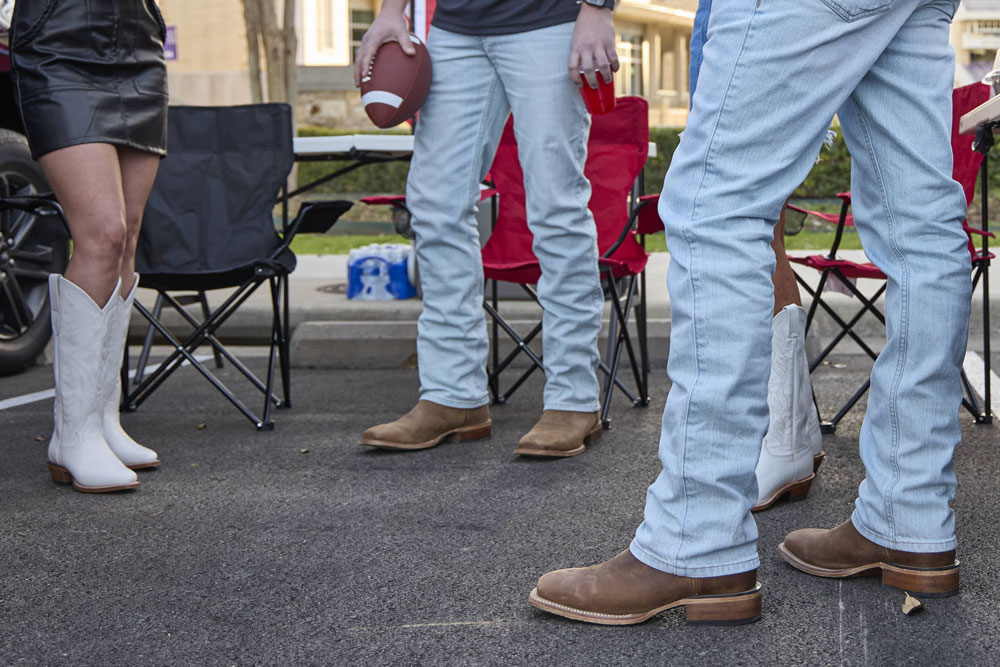 A group of young adults wearing Justin Boots while tailgating at a football game.